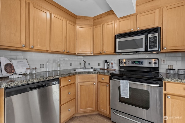 kitchen featuring appliances with stainless steel finishes, light hardwood / wood-style floors, backsplash, dark stone counters, and sink