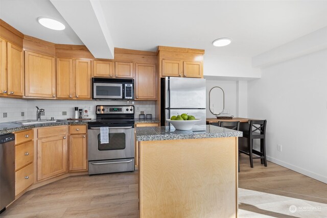 kitchen with appliances with stainless steel finishes, light hardwood / wood-style floors, tasteful backsplash, a center island, and sink