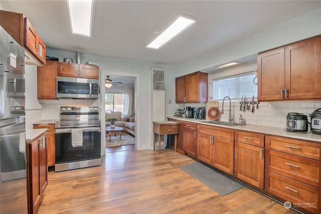 kitchen featuring tasteful backsplash, appliances with stainless steel finishes, sink, light hardwood / wood-style floors, and ceiling fan