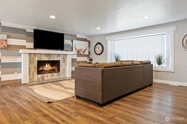 living room with a tiled fireplace, a textured ceiling, and hardwood / wood-style floors