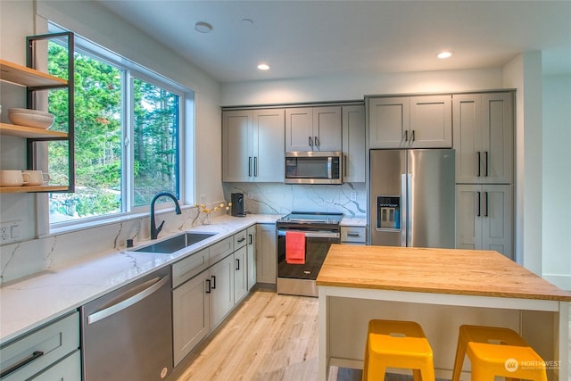 kitchen with sink, tasteful backsplash, appliances with stainless steel finishes, light stone countertops, and light hardwood / wood-style floors