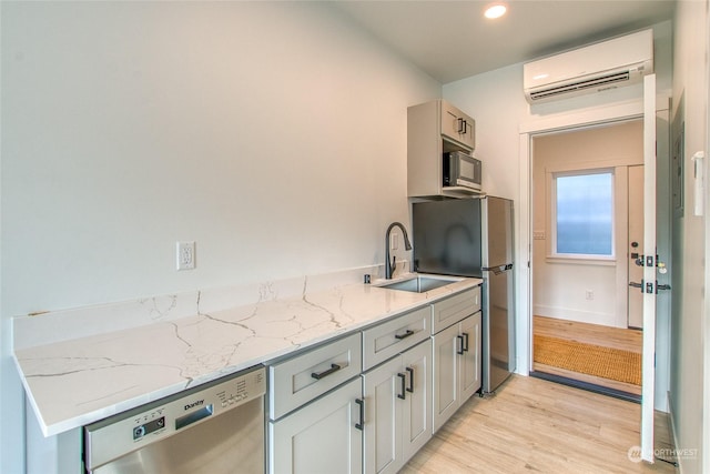 kitchen featuring sink, stainless steel dishwasher, light hardwood / wood-style floors, light stone countertops, and a wall unit AC