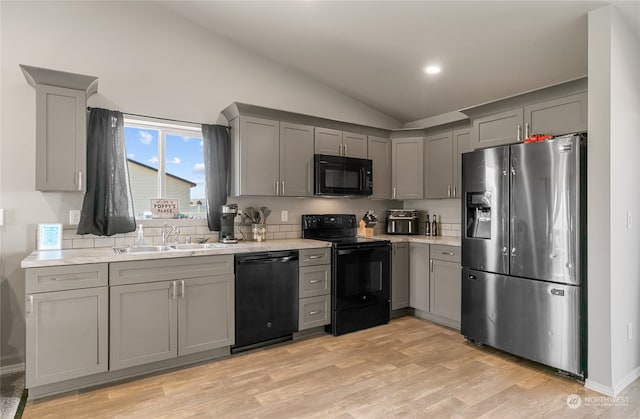 kitchen with gray cabinetry, light wood-type flooring, black appliances, lofted ceiling, and sink