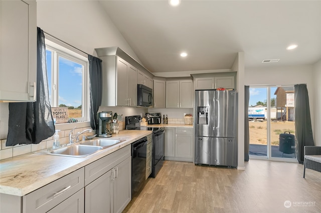 kitchen featuring lofted ceiling, sink, gray cabinetry, black appliances, and light hardwood / wood-style floors