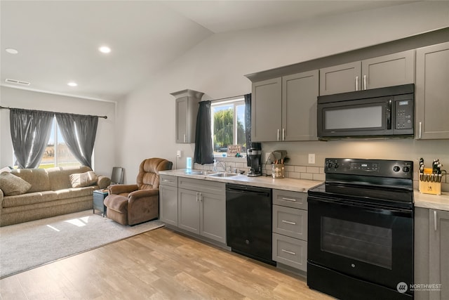 kitchen with light hardwood / wood-style floors, vaulted ceiling, gray cabinets, black appliances, and sink