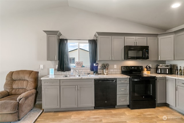 kitchen with gray cabinets, light hardwood / wood-style floors, vaulted ceiling, and black appliances