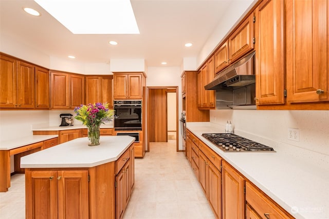 kitchen featuring light countertops, under cabinet range hood, a kitchen island, stainless steel gas stovetop, and brown cabinets