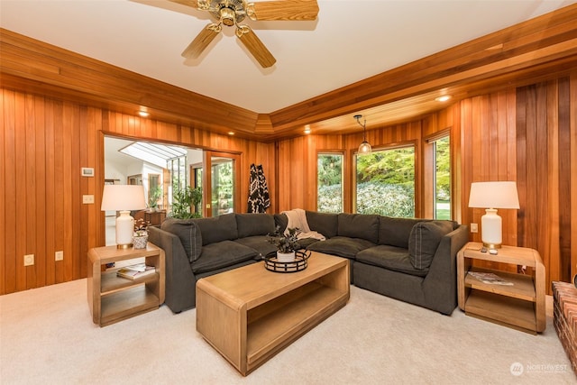 living room featuring wood walls, a healthy amount of sunlight, a ceiling fan, and light carpet