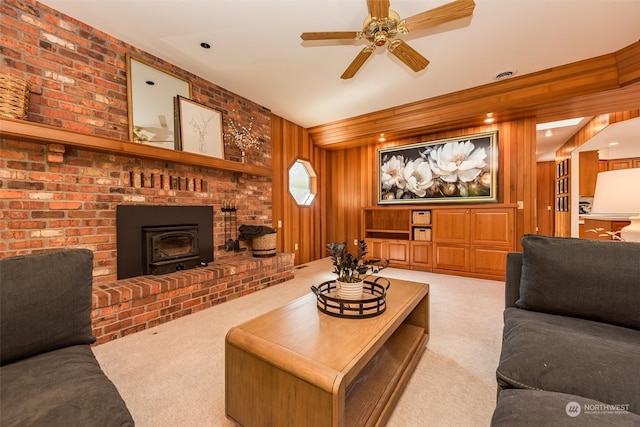 living room with wood walls, a wood stove, carpet flooring, and a ceiling fan