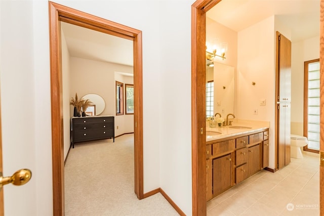 bathroom featuring toilet, a sink, double vanity, and baseboards