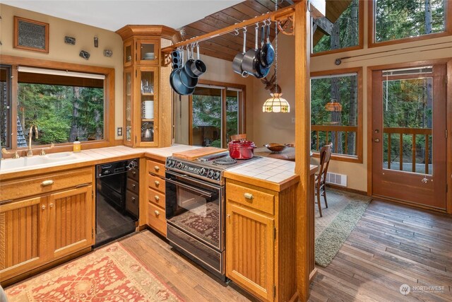 kitchen featuring a sink, tile counters, light wood-style flooring, visible vents, and black appliances