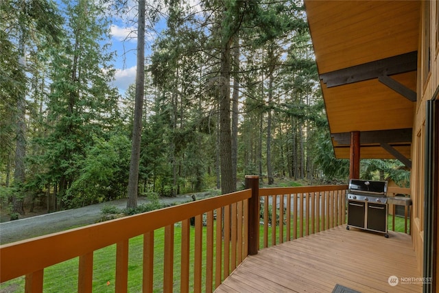 wooden terrace featuring a lawn, a forest view, and a grill