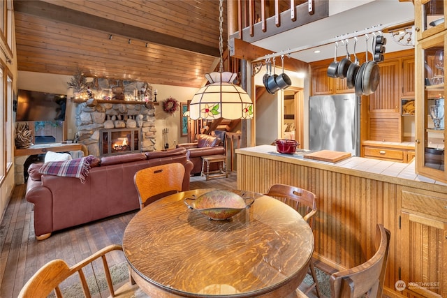 dining area featuring dark hardwood / wood-style flooring, a stone fireplace, wood ceiling, and lofted ceiling with beams