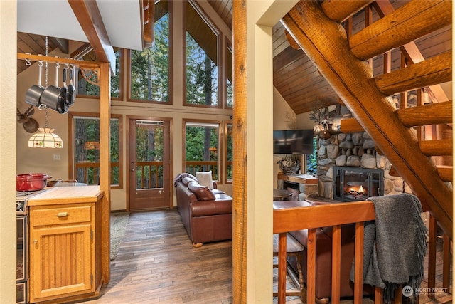 interior space with wood-type flooring, beam ceiling, a stone fireplace, and high vaulted ceiling