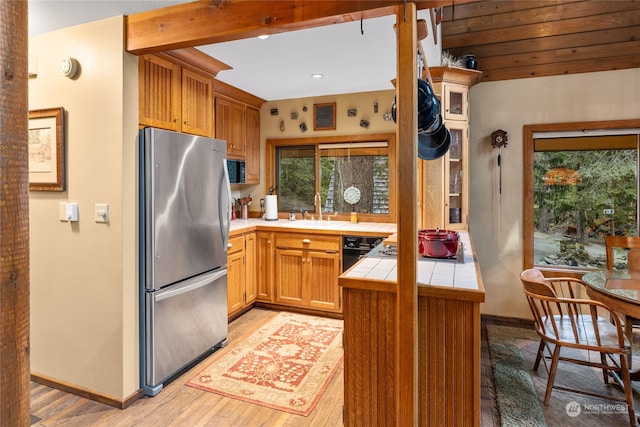 kitchen with tile countertops, kitchen peninsula, stainless steel fridge, light wood-type flooring, and sink