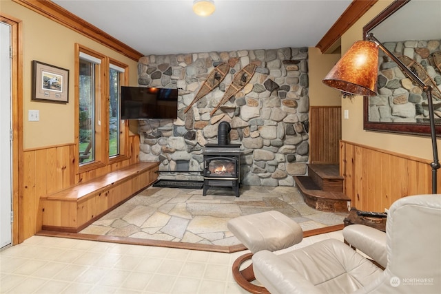 living room featuring crown molding, a wood stove, a wainscoted wall, and wooden walls