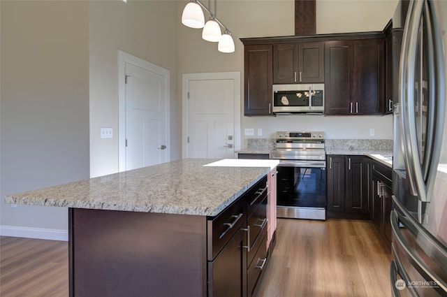 kitchen with wood-type flooring, a center island, appliances with stainless steel finishes, and decorative light fixtures