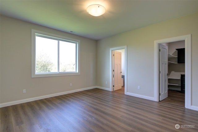 unfurnished bedroom with a closet, dark hardwood / wood-style flooring, and a spacious closet