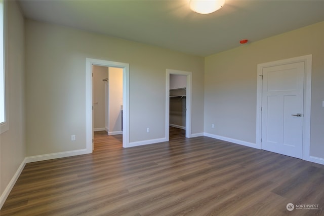 unfurnished bedroom featuring dark hardwood / wood-style flooring, a walk in closet, and a closet