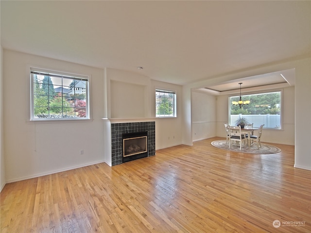 unfurnished living room with a notable chandelier, plenty of natural light, light hardwood / wood-style floors, and a tile fireplace