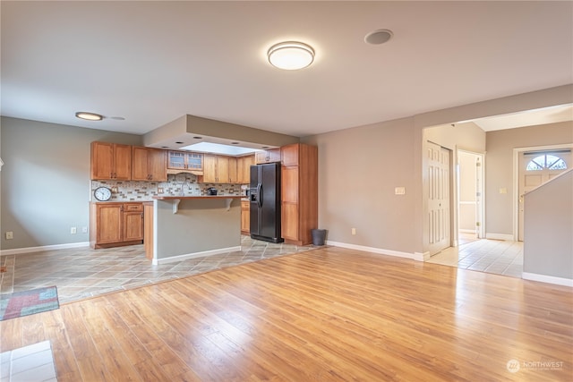 kitchen featuring tasteful backsplash, a kitchen bar, a center island, black fridge, and light hardwood / wood-style flooring