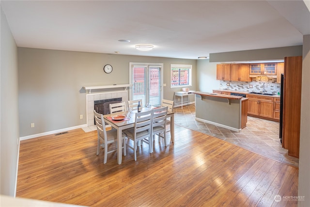 dining area featuring sink, light hardwood / wood-style flooring, and a tile fireplace