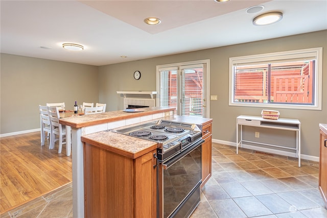 kitchen with light hardwood / wood-style floors, black electric range oven, a tiled fireplace, and a kitchen island