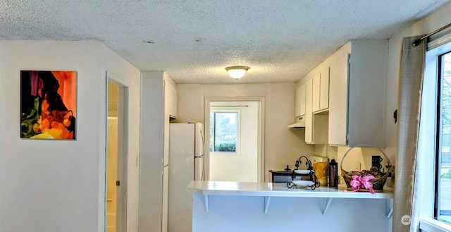 kitchen featuring a kitchen breakfast bar, a healthy amount of sunlight, white cabinets, and white refrigerator