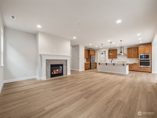 unfurnished living room with light hardwood / wood-style floors, a stone fireplace, and sink