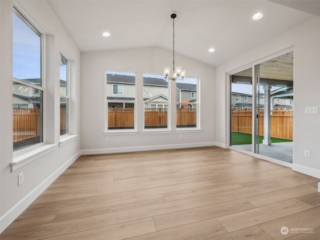 unfurnished dining area featuring an inviting chandelier, vaulted ceiling, and light hardwood / wood-style floors