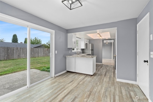 kitchen with light hardwood / wood-style flooring, white cabinetry, sink, and stainless steel fridge