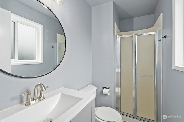 bathroom featuring vanity, a shower with shower door, and toilet