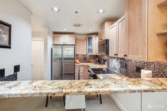 kitchen with stainless steel appliances, light brown cabinetry, a breakfast bar, and kitchen peninsula