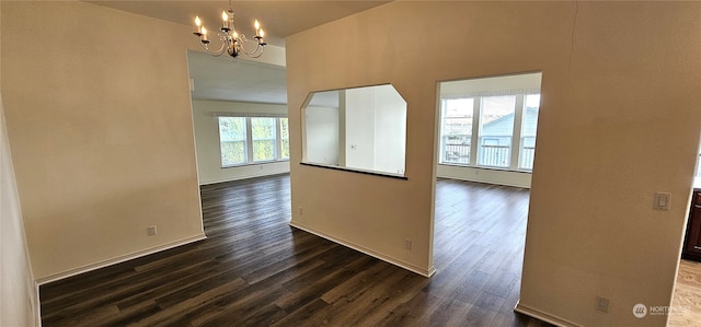 spare room featuring an inviting chandelier, dark wood-type flooring, and a healthy amount of sunlight