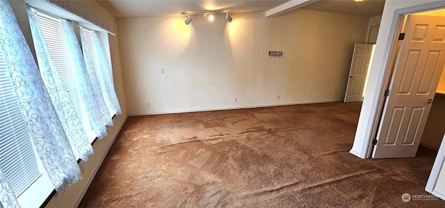 unfurnished bedroom featuring dark carpet, beam ceiling, and track lighting