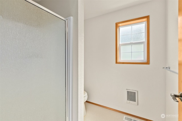 bathroom with heating unit, toilet, and an enclosed shower