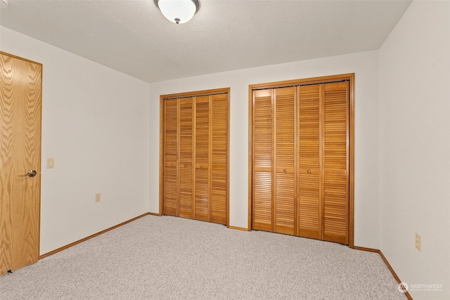 unfurnished bedroom featuring multiple closets, a textured ceiling, and carpet