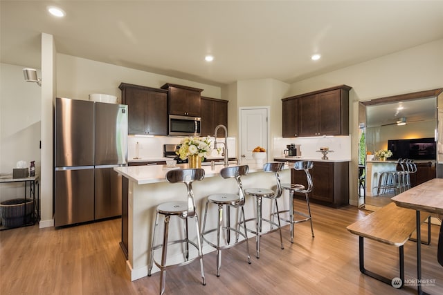 kitchen featuring light wood-type flooring, a kitchen island with sink, sink, stainless steel appliances, and dark brown cabinetry