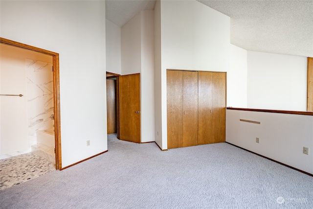 unfurnished bedroom with connected bathroom, a textured ceiling, high vaulted ceiling, a closet, and light carpet