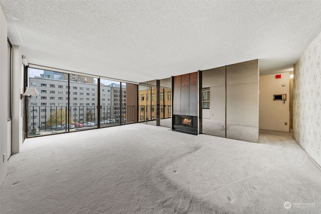 unfurnished living room featuring light carpet, a wall of windows, a multi sided fireplace, and a textured ceiling