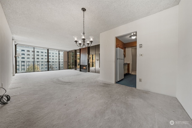 carpeted empty room with a textured ceiling, an inviting chandelier, and expansive windows