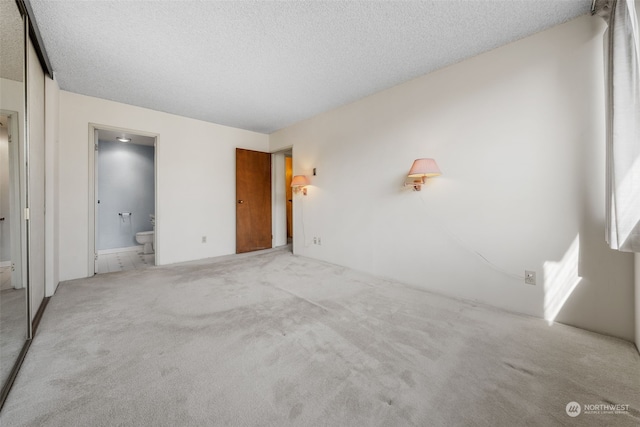 unfurnished bedroom with light carpet, a textured ceiling, a closet, and connected bathroom