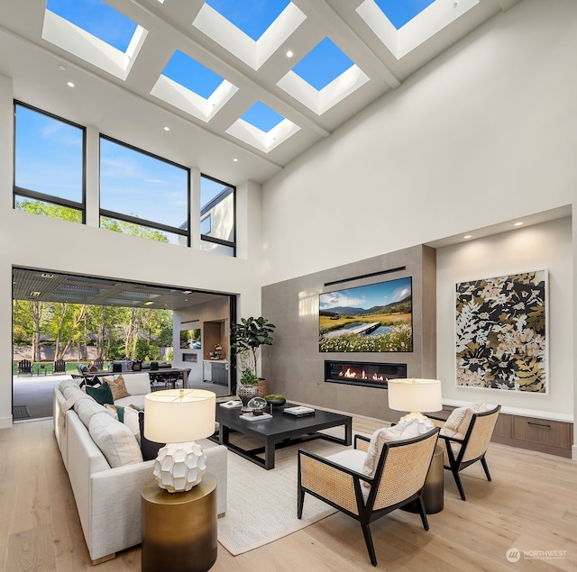 living room with light wood-type flooring, a high ceiling, and a skylight