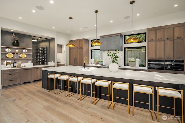 kitchen with a kitchen breakfast bar, hanging light fixtures, light wood-type flooring, and stainless steel oven