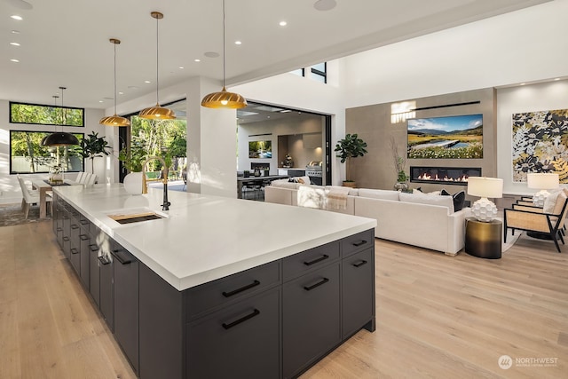 kitchen with a large island with sink, sink, light hardwood / wood-style flooring, and decorative light fixtures