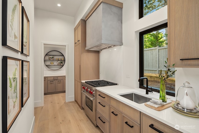 kitchen with light wood-type flooring, wall chimney exhaust hood, designer range, and sink