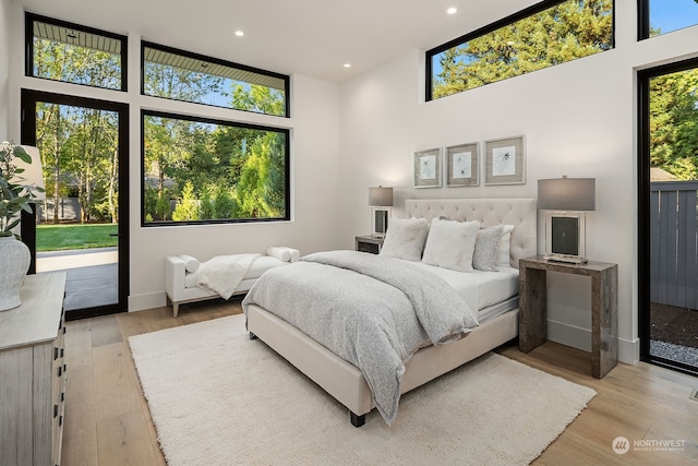 bedroom with multiple windows, light wood-type flooring, and a towering ceiling