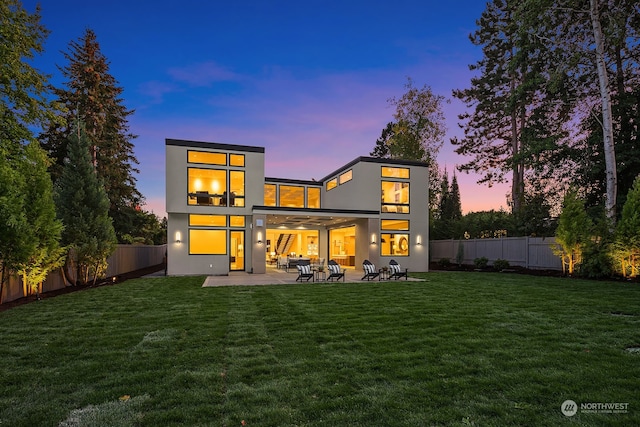 back house at dusk featuring a lawn and a patio