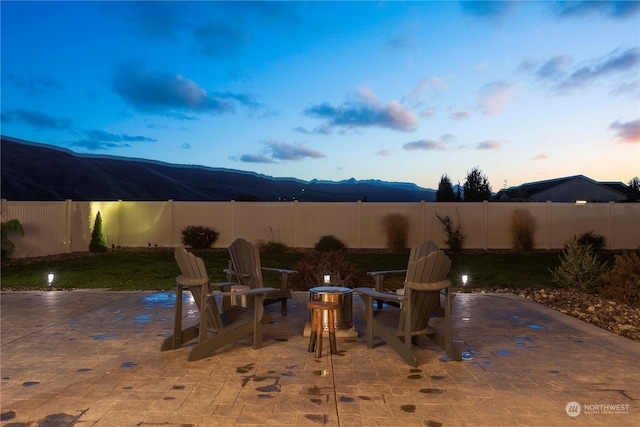 pool at dusk with an outdoor fire pit, a mountain view, and a patio