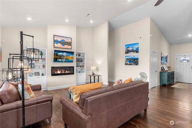 living area featuring dark wood-style floors, a glass covered fireplace, and lofted ceiling